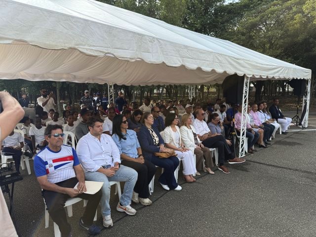 Asistentes sentados bajo una carpa blanca junto a las canchas.