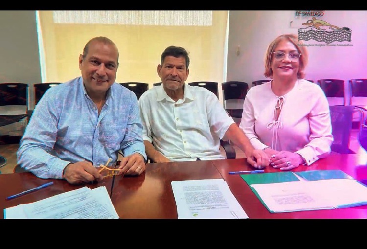 Tres personas posan sentadas a una mesa con documentos.