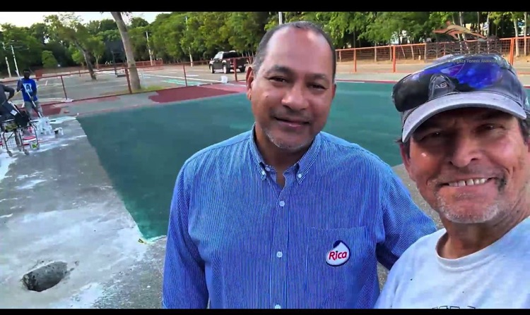 Dos hombres posan juntos junto a una cancha de tenis.