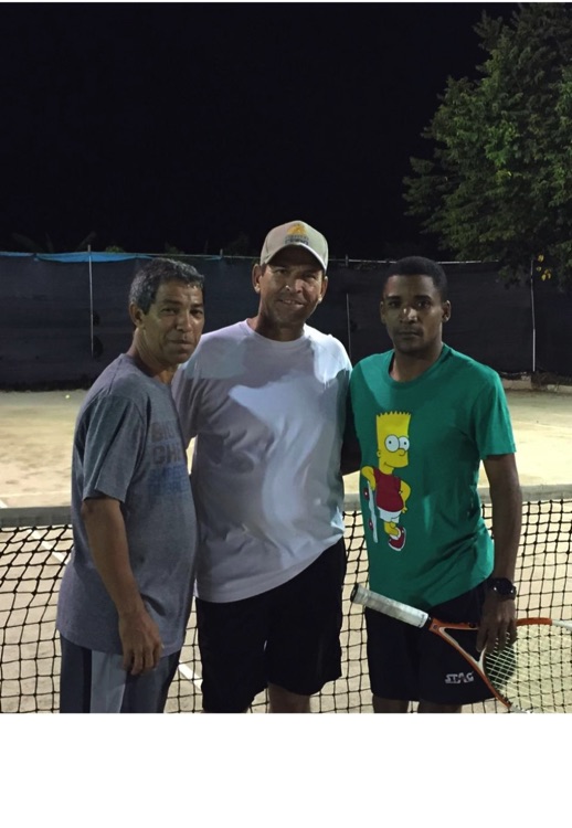 Tres participantes posan juntos en una cancha de tenis por la noche.