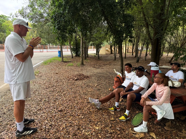 Instructor habla con un grupo sentado a la sombra de los árboles.