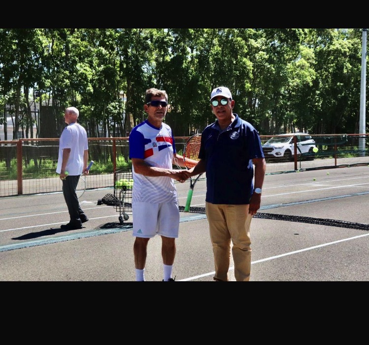 Dos hombres posan juntos en una cancha de tenis al aire libre.