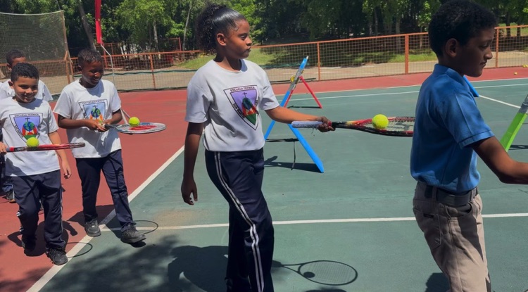 Niños practican con raquetas y pelotas durante una clase de tenis.