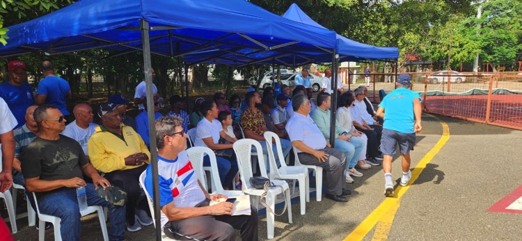 Asistentes reunidos bajo una carpa azul junto a las canchas de tenis.