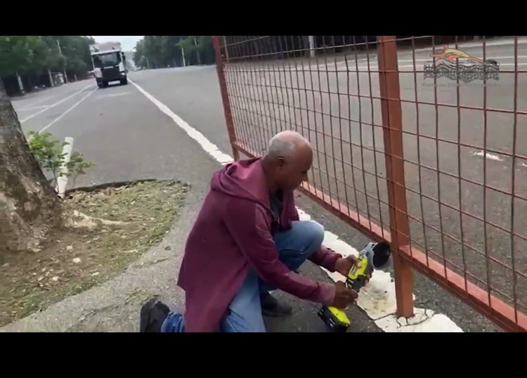 Un hombre atiende material deportivo junto a la valla de la cancha.